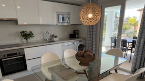 A modern kitchen with white cabinets, a built-in microwave, and a glass dining table with white chairs. - Nerja Paradise Rentals - Villa Las Palmeras (Nerja)