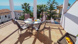 Un balcon avec une table dressée pour deux personnes, entouré de chaises, donnant sur une piscine et des palmiers.