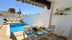 Un espace repas aménagé au bord de la piscine, avec une table dressée pour deux personnes, des chaises et une vue sur la piscine.