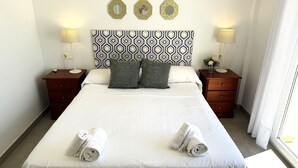 Un lit bien fait, avec deux serviettes enroulées, une tête de lit à motifs, des tables de chevet avec des lampes et une fenêtre avec des rideaux.