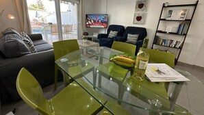 Un salon moderne avec une table à manger en verre, des chaises vertes, un canapé gris et un téléviseur.