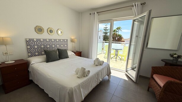 Une chambre d’hôtel avec un grand lit, une table de chevet, une commode, une chaise et un balcon équipé d’une table et de chaises.