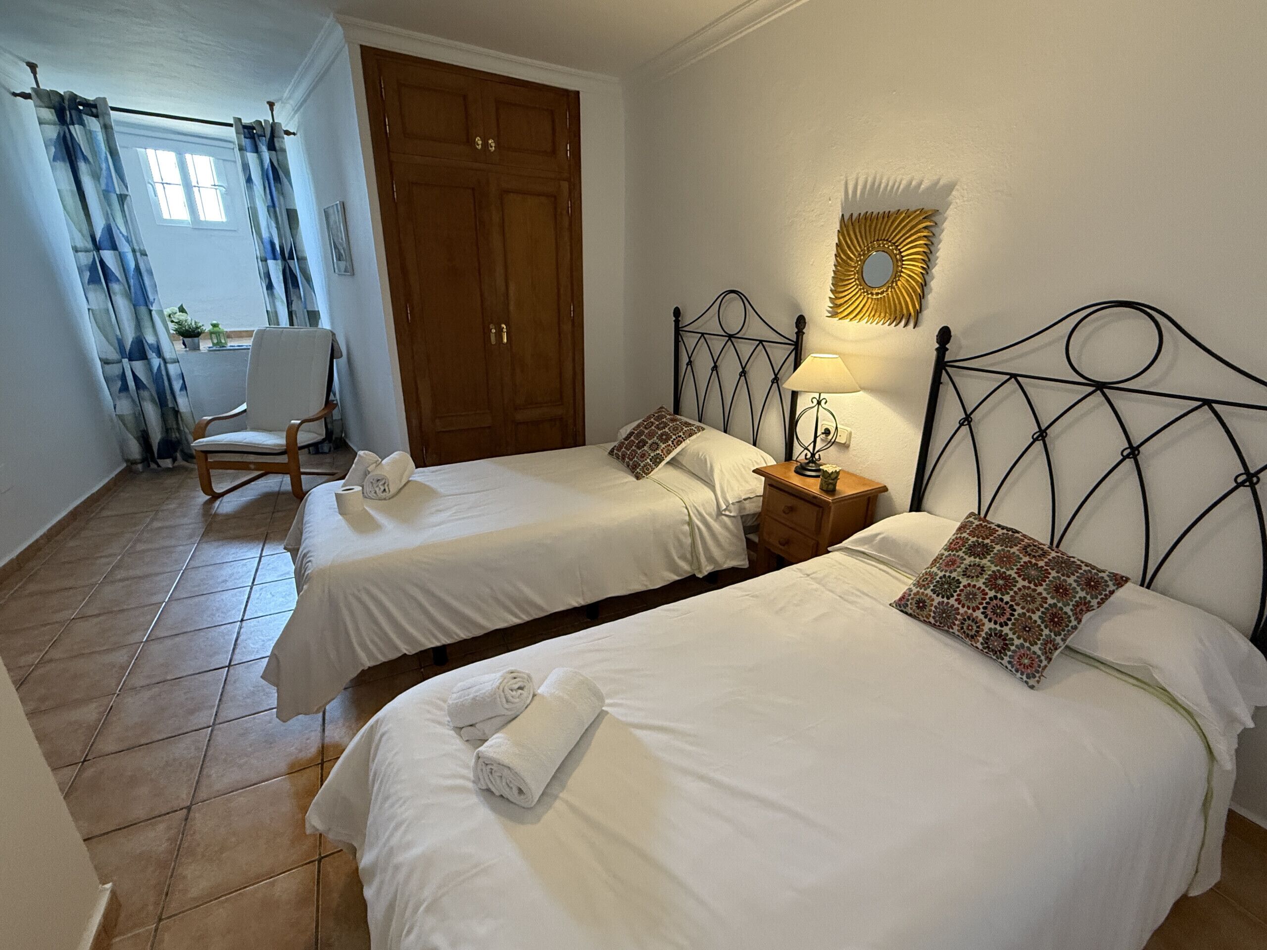 Une chambre d’hôtel avec deux lits simples, une armoire en bois, une chaise et une petite table avec une lampe.