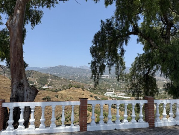 Balcón con barandilla blanca que da a un paisaje montañoso con viñedos y montañas a lo lejos.