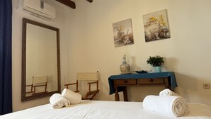 Ein Hotelzimmer mit einem großen Spiegel, zwei Bildern, einem Holzstuhl, einem kleinen Tisch mit einer Vase und Pflanze sowie Handtüchern auf dem Bett.