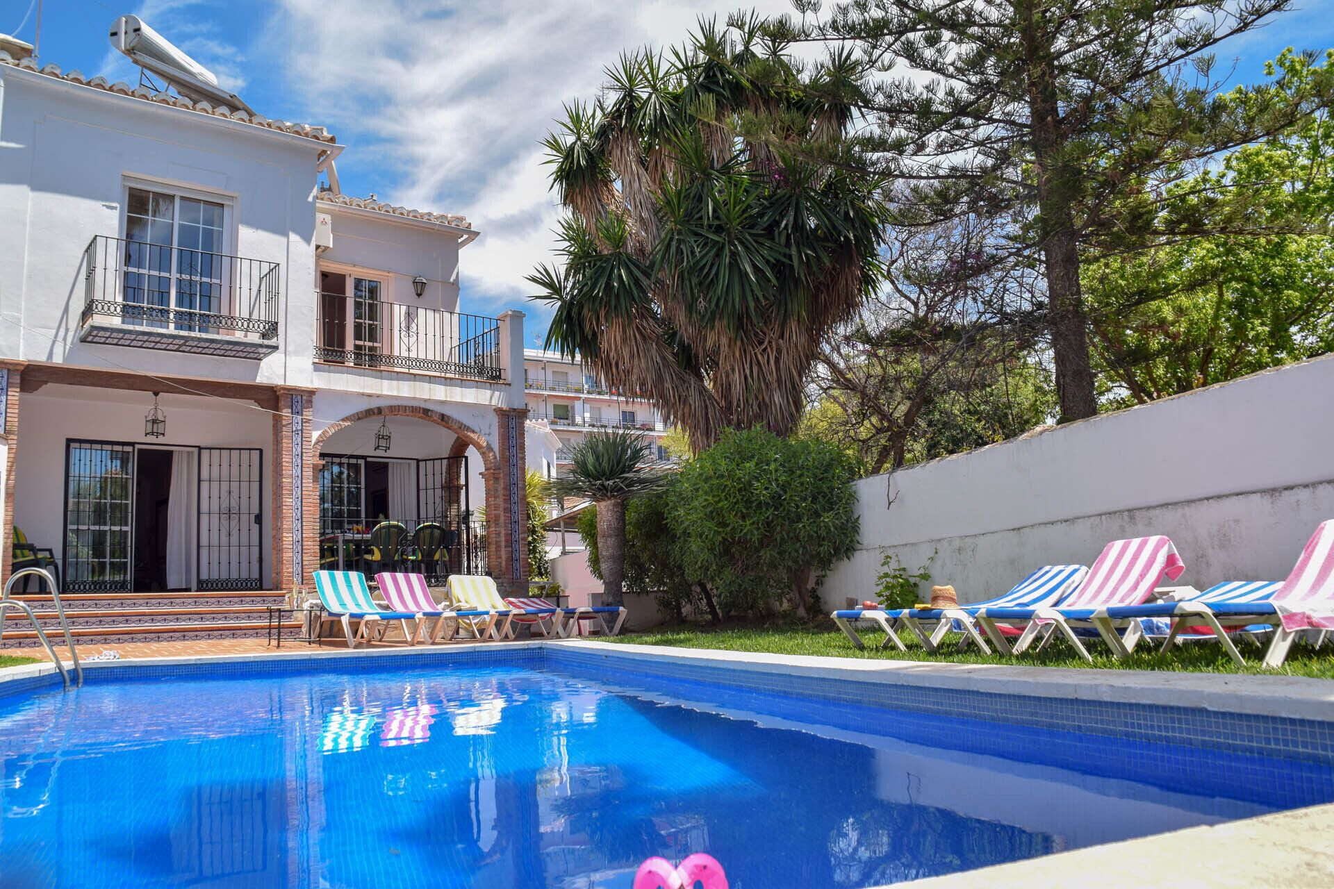 A pool area with lounge chairs, a clear blue pool, and a two-story building with balconies.