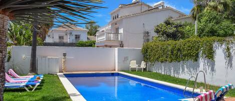 A swimming pool with lounge chairs and a tiled deck.