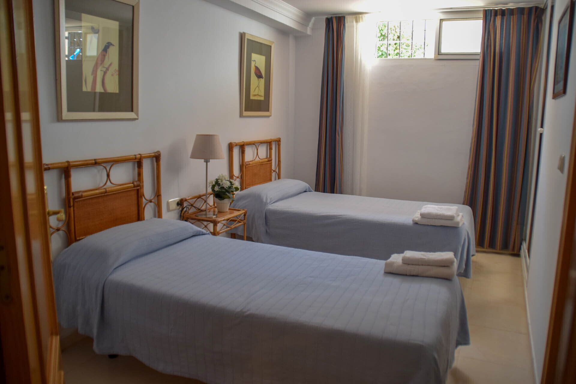 Une chambre d’hôtel avec deux lits simples, une table de chevet avec une lampe et une fenêtre avec des rideaux.