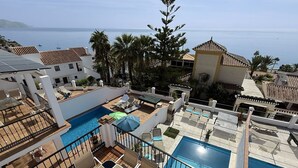 Un área de piscina en la azotea con varias piscinas, sillas de descanso y sombrillas.