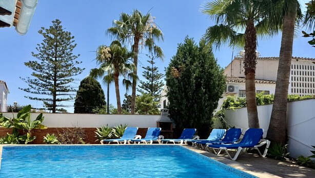 A swimming pool with blue water, surrounded by palm trees and lounge chairs. - Nerja Paradise Rentals - Villa Jazmines (Nerja)