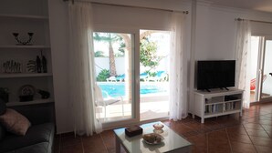 A living room with a TV, a glass coffee table, and a pool view. - Nerja Paradise Rentals - Villa Jazmines (Nerja)