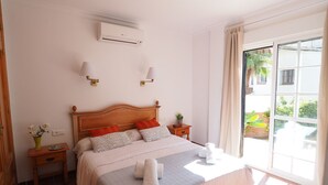 A hotel room with a bed, a nightstand, a wall-mounted air conditioner, and a view of the outdoors through a sliding glass door. - Nerja Paradise Rentals - Villa Jazmines (Nerja)