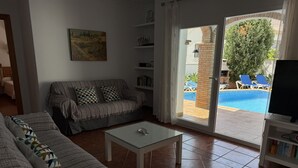 A living room with a sofa, a coffee table, and a TV stand. There is a sliding glass door leading to a pool area. - Nerja Paradise Rentals - Villa Jazmines (Nerja)