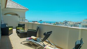 Un balcón con sillones de sol y una mesa, con vistas a la costa.