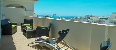 Un balcon doté de chaises longues et d’une table, offrant une vue sur la côte.