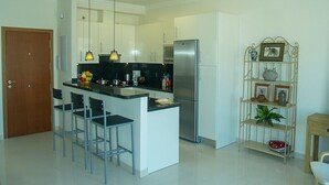 Una cocina moderna con una isla central, taburetes de bar, un refrigerador de acero inoxidable, luces colgantes y una repisa metálica decorativa.