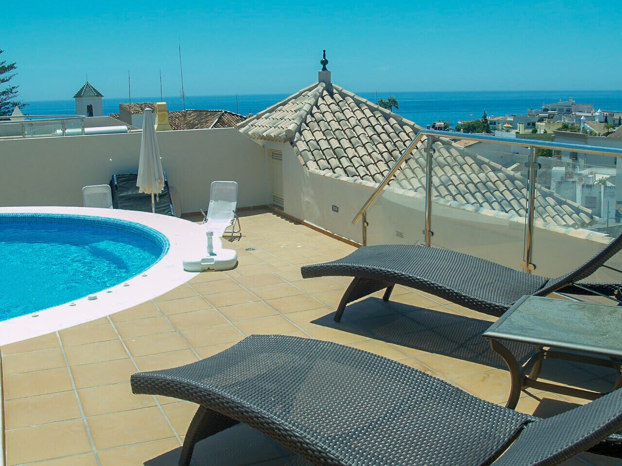 A rooftop pool area with lounge chairs and a view of the sea.