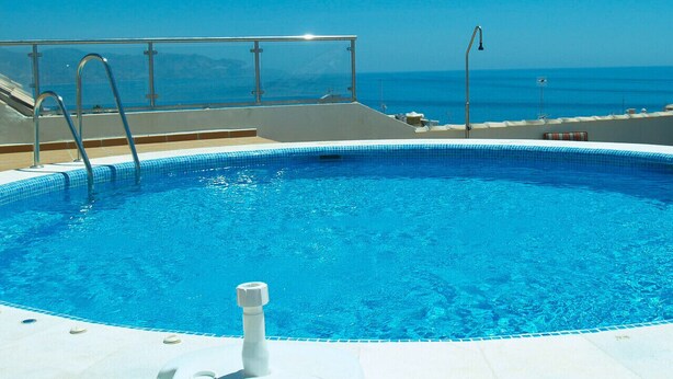 Una piscina azul cristalina con escalones de acceso, rodeada por una terraza.