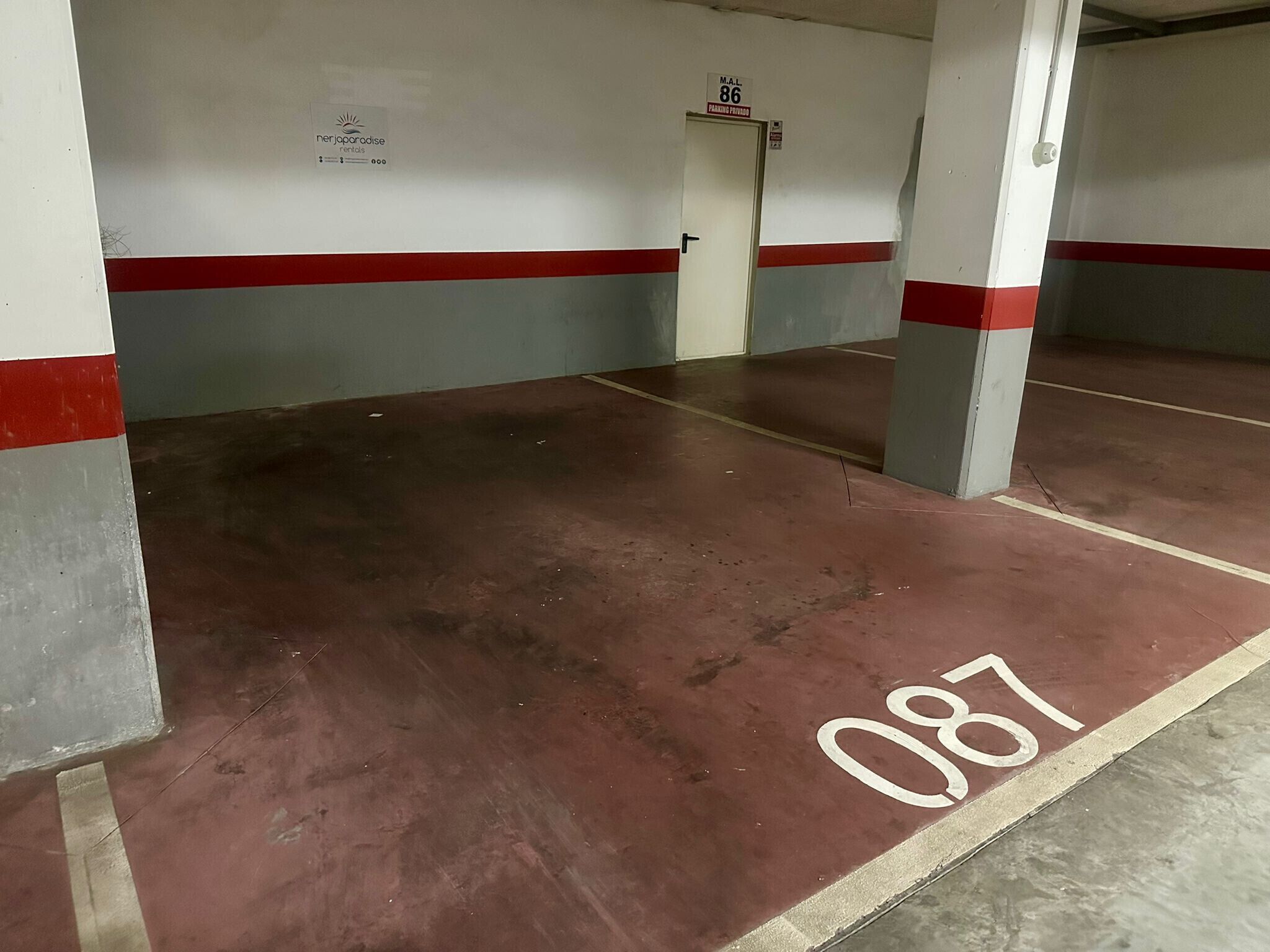 Een parkeergarage met betonnen vloeren en rode en grijze wanden.