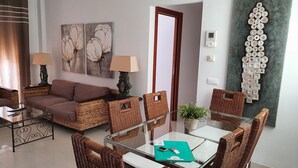 Una sala de estar moderna con una mesa de comedor de cristal, mobiliario de mimbre y una gran obra de arte abstracta en la pared.