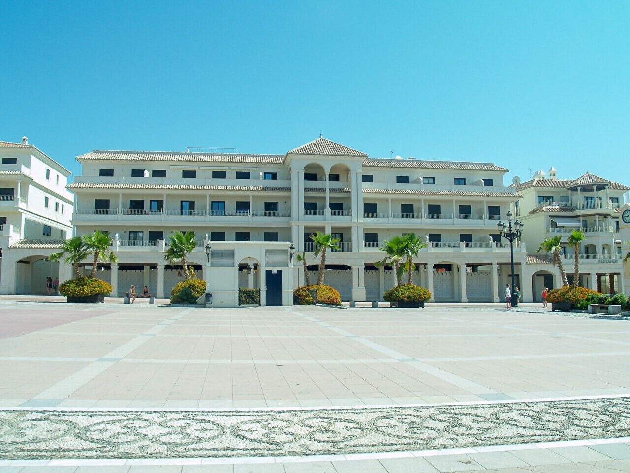 A large, multi-story hotel with a central courtyard, palm trees, and a tiled floor.