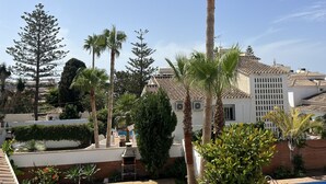 Zona residencial amb piscina, palmeres i un edifici blanc amb teulada enrajolada.