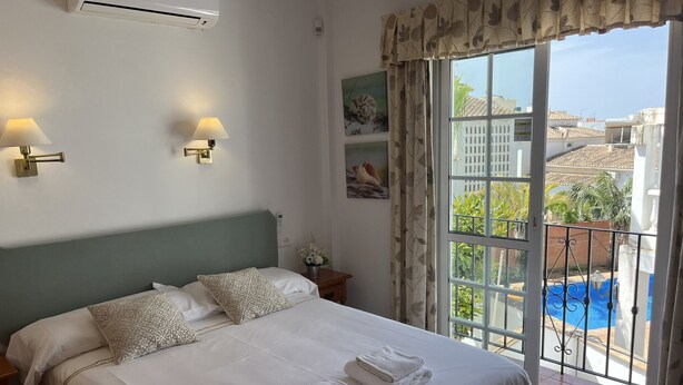 Habitació d'hotel amb llit, dues làmpades penjades a la paret, finestra amb vista a una piscina i edificis, i un aparell d'aire condicionat.