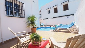 Zona de piscina amb gandules, una taula petita amb una planta en test i un paviment de rajoles.
