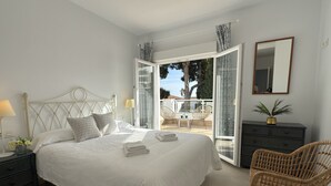Une chambre à coucher comprenant un lit, une table de chevet, une lampe et donnant sur un balcon extérieur.