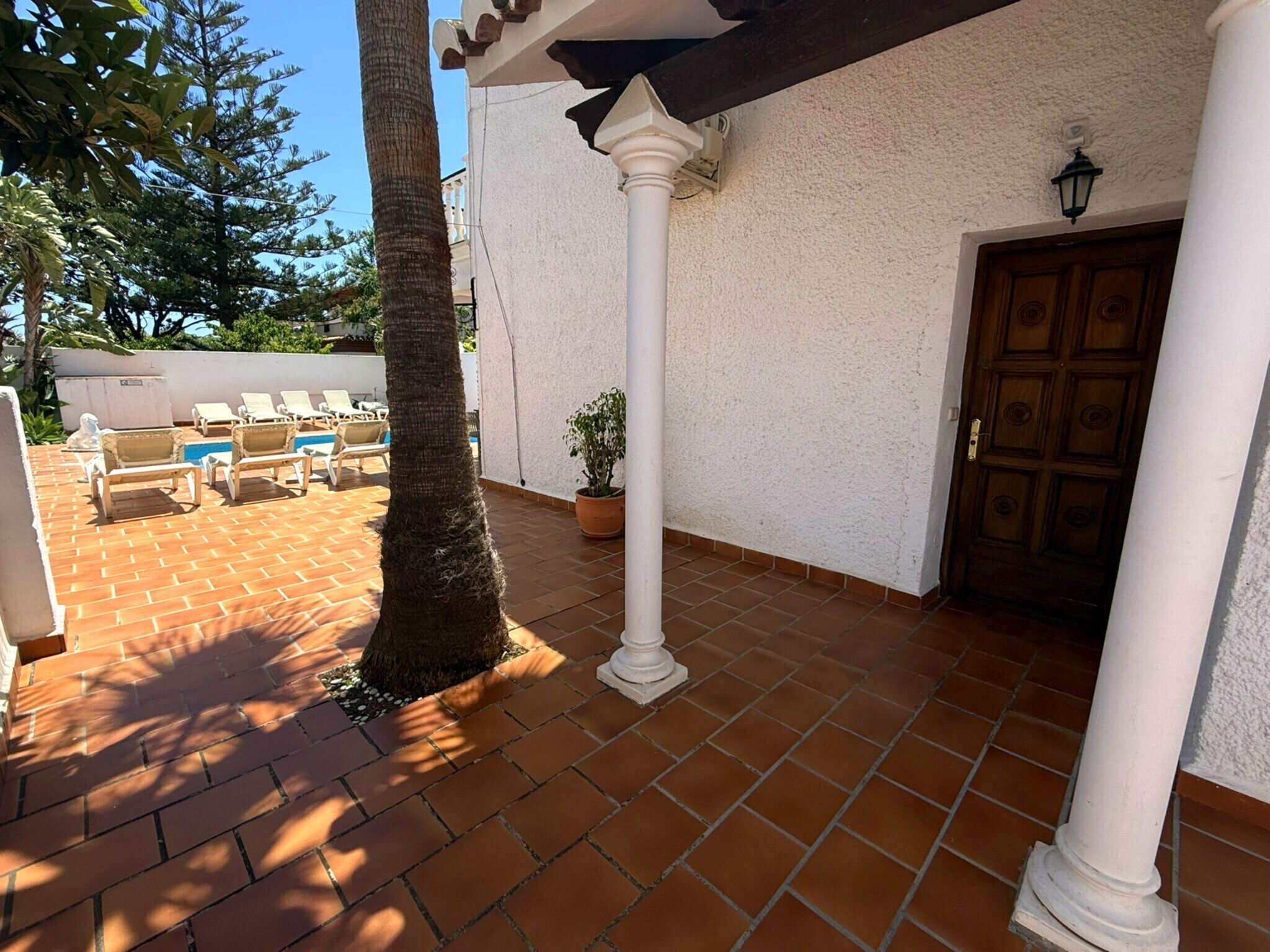 Un espace patio agrémenté d’une colonne blanche, d’une porte en bois et d’un sol carrelé.