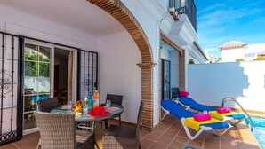 A patio with a table, chairs, and a pool area with lounge chairs.