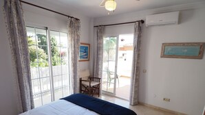 A bedroom with a bed, a chair, a table, and a view through a sliding glass door.