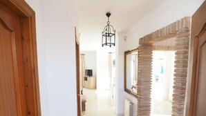 A hallway with a wooden door, a mirror with a brick-like frame, and a hanging light fixture.