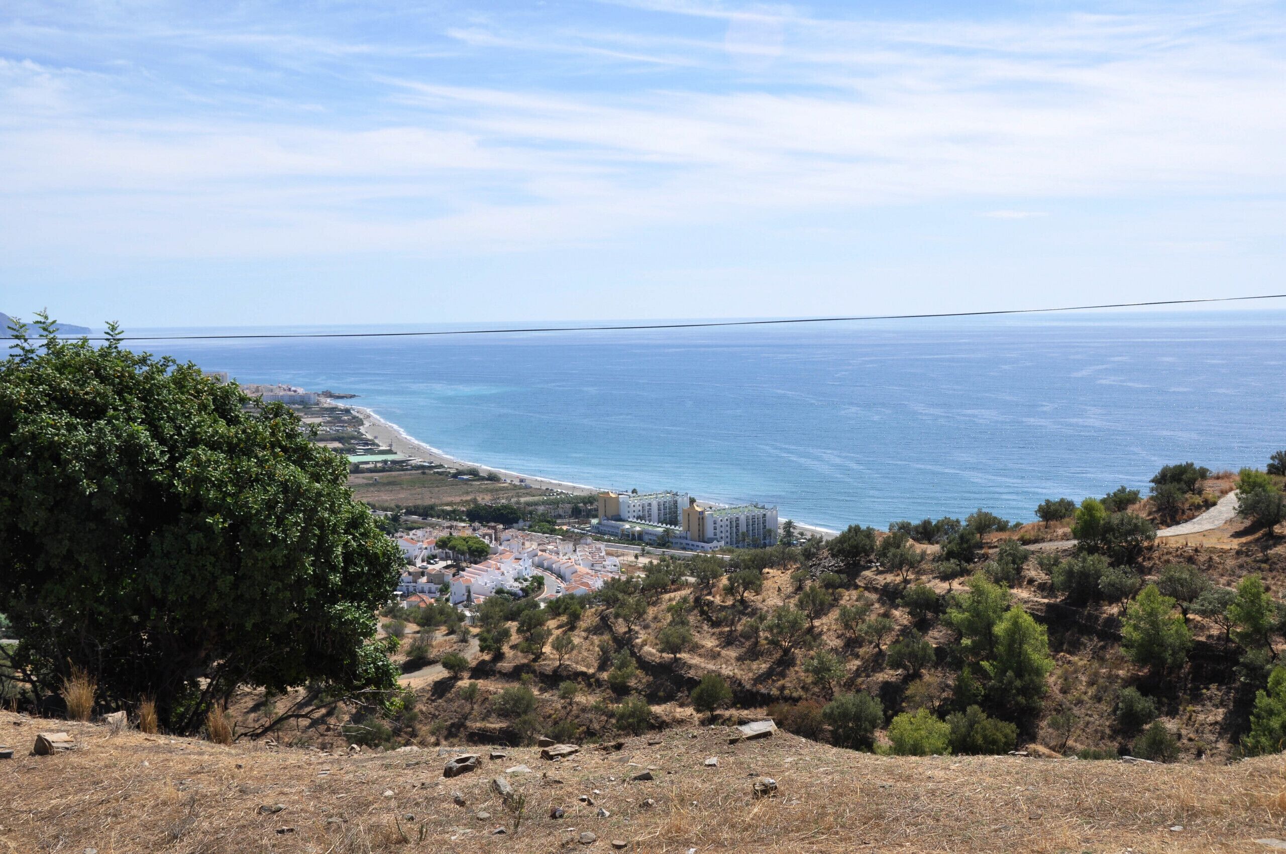 Blick auf die Küste mit Strand, einer kleinen Stadt und einem Hügel mit spärlicher Vegetation.