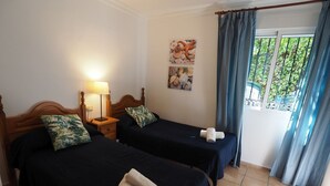 A hotel room with two beds, a nightstand with a lamp, a window with curtains, and a wall with a picture. - Nerja Paradise Rentals - Villa Los Girasoles (Nerja)
