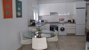 A modern kitchen with white cabinets, a glass dining table, and a washing machine. - Nerja Paradise Rentals - Villa Valeria (Nerja)