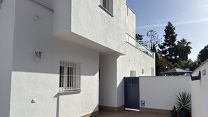 A modern building with a flat facade, a gated entrance, and a small courtyard with wooden flooring. - Nerja Paradise Rentals - Villa Valeria (Nerja)