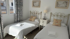 A hotel room with two single beds, a small bedside table with a lamp, and a window with curtains. - Nerja Paradise Rentals - Villa Valeria (Nerja)