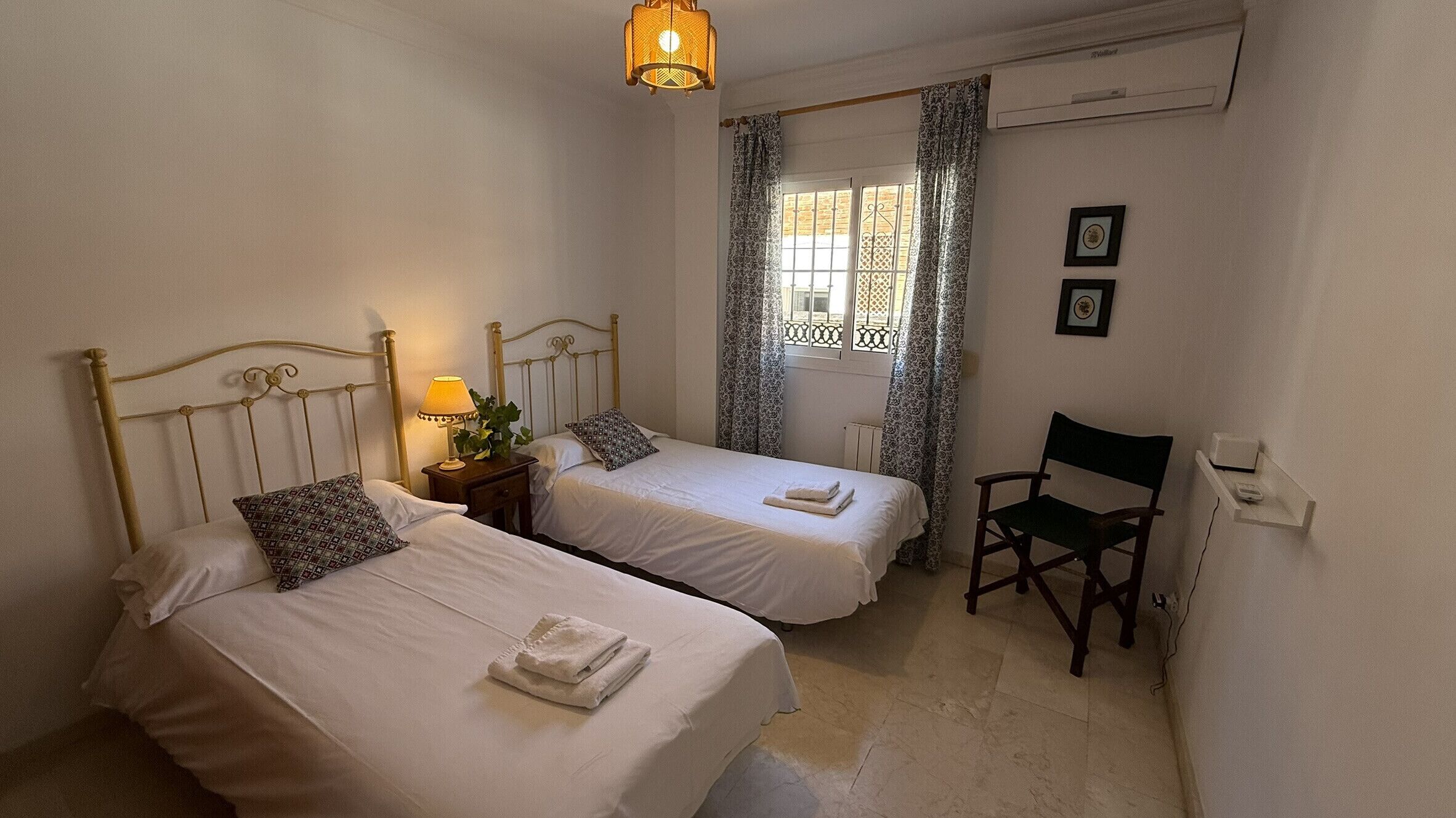 Una habitación con dos camas, una silla, una lámpara y un equipo de aire acondicionado.