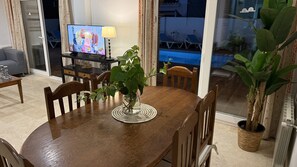 A dining area with a wooden table, chairs, a TV, and a view of a swimming pool. - Nerja Paradise Rentals - Villa Las Dalias (Nerja)