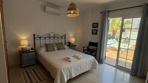 Un dormitorio con cama, dos mesitas de noche, una lámpara colgante, una ventana con cortinas y vistas al exterior.