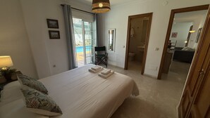 Un dormitorio con cama, una silla, un escritorio y vista a una piscina exterior.
