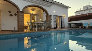 A swimming pool with a patio area, a dining table with chairs, and a view of a building with a tiled roof. - Nerja Paradise Rentals - Villa Las Dalias (Nerja)