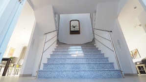 Una escalera moderna con barandilla de vidrio que conduce a un rellano con un espejo.