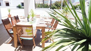 Una terraza en la azotea con una mesa y sillas de madera, plantas en macetas y vistas de la ciudad.