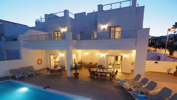Un edificio de dos pisos con piscina, zona de comedor al aire libre y sillas de descanso.
