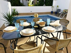 A dining table set for six with plates, glasses, and cutlery, surrounded by wicker chairs, with a pool in the background. - Nerja Paradise Rentals - Villa Bonilla (Nerja)