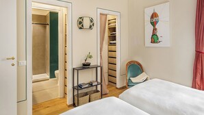 Habitación de hotel con dos camas, una mesita con una planta, un armario y un cuadro en la pared.