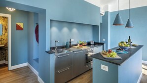 Una cocina moderna con paredes azules, electrodomésticos de acero inoxidable y una isla central con frutas y vino.
