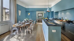Una cocina moderna con una isla central, un comedor con sillas transparentes y vistas a la ciudad a través de amplios ventanales.